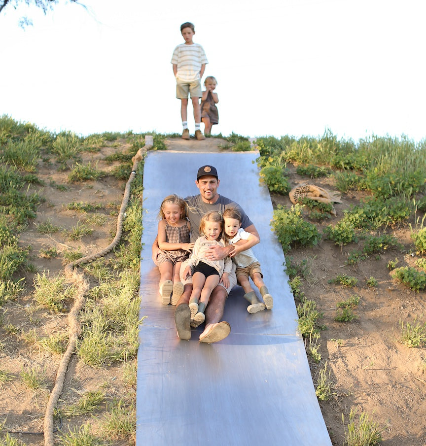 Family enjoying outdoor activities on a farm, highlighting Primal Pastures' commitment to sustainable farming and grass-fed meats, with lush greenery in the background.