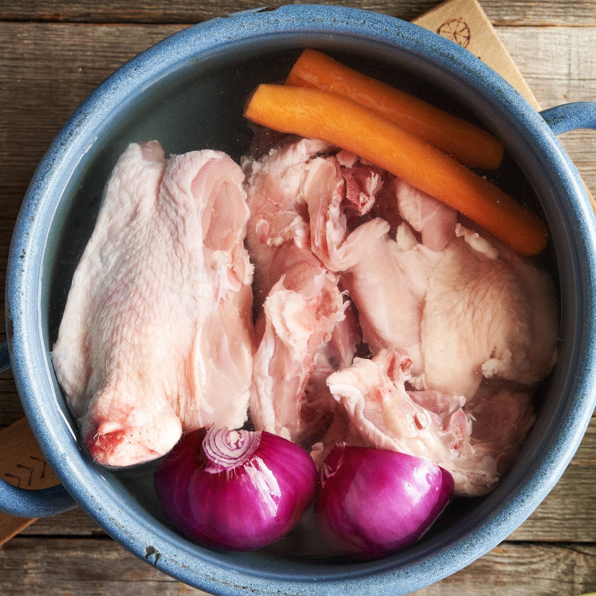 A pot containing chicken bones, carrots, and onions, presumably being prepared for broth making.