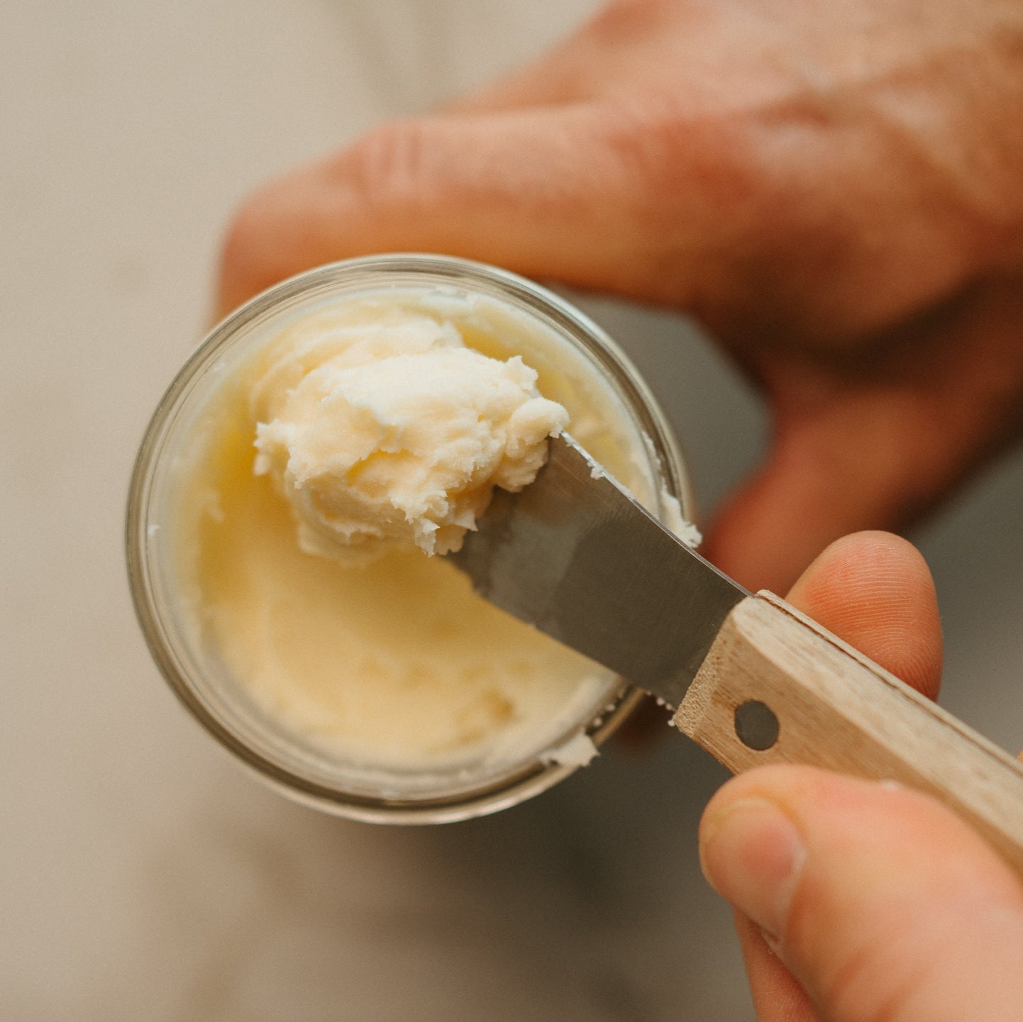 Hand scooping beef tallow from a glass jar with a butter knife.