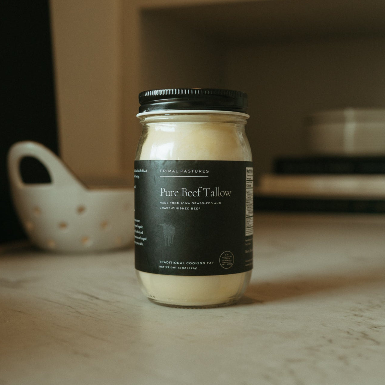 Jar of Primal Pastures Pure Beef Tallow on a smooth surface, featuring a black label with gold & white text.