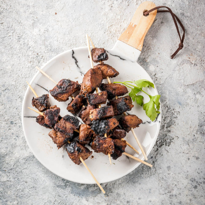 Grilled skewers of grass-fed beef liver served on a white plate with a garnish of fresh herbs.
