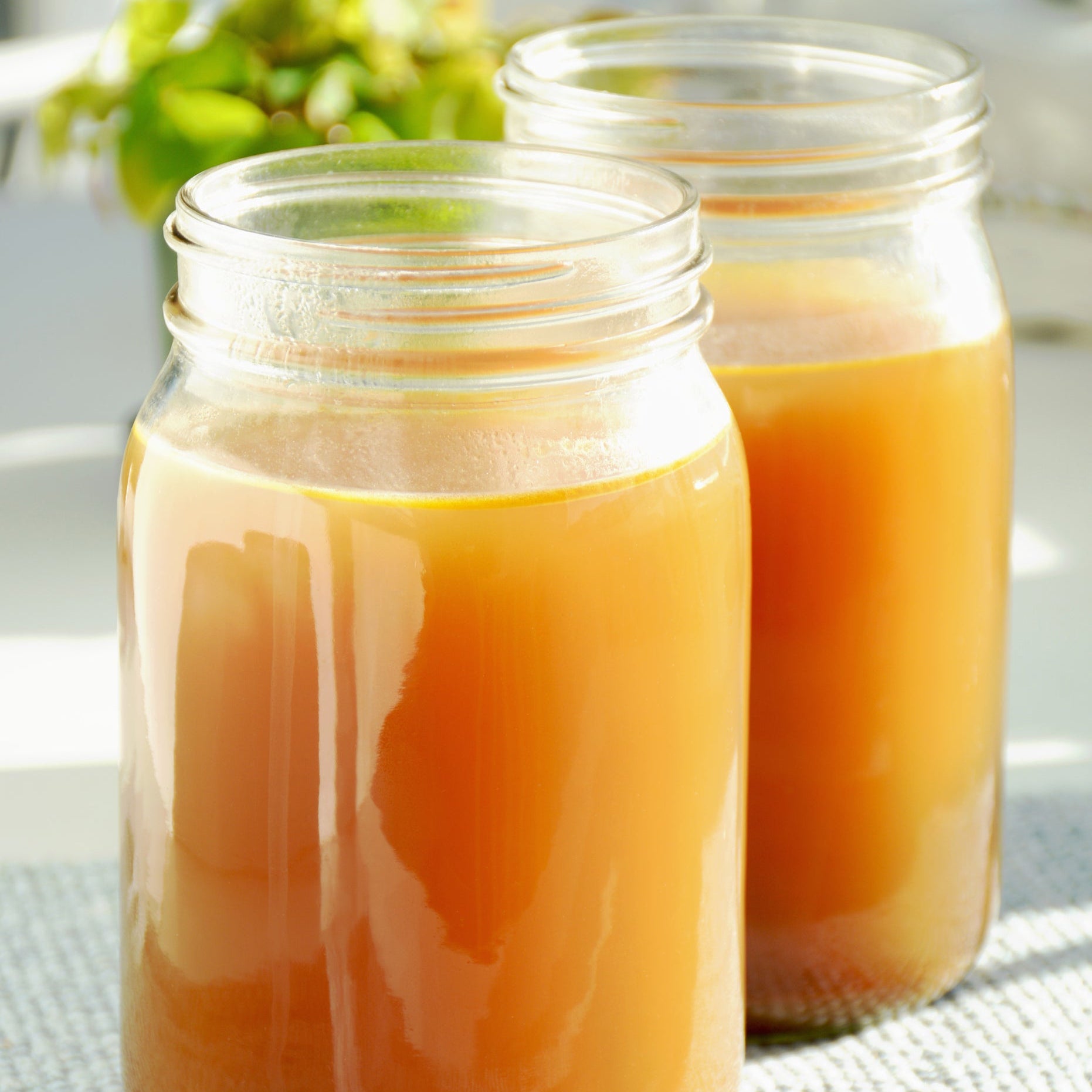 Two glass jars filled with chicken bone broth, placed on a kitchen counter with a bundle of parsley in the background.