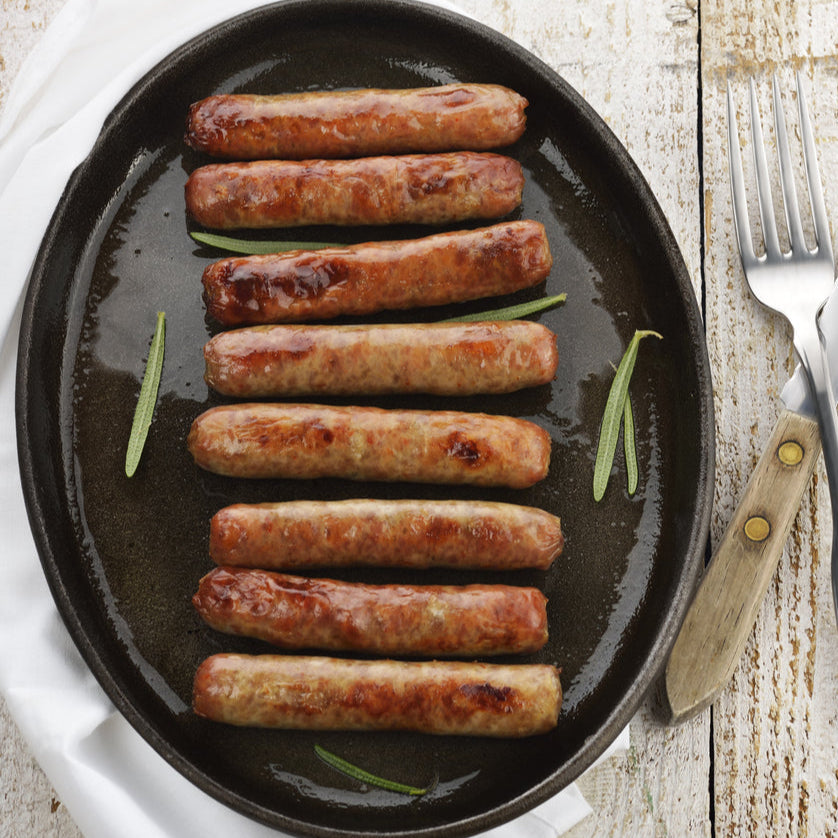 A plate with cooked pork breakfast sausage links garnished with rosemary sprigs, with a fork and knife on the side.