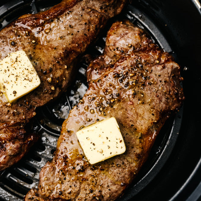 Two flat iron steaks on a grill pan with visible grill marks and pieces of butter on top.