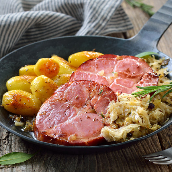 Sliced ham steaks in a skillet with potatoes and herbs.