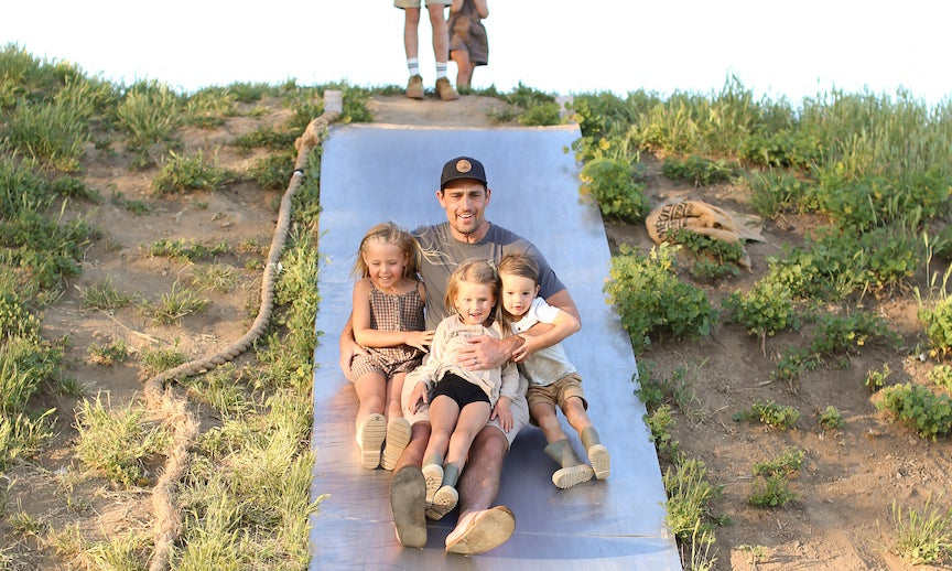 Family enjoying outdoor activities on a farm, highlighting Primal Pastures' commitment to sustainable farming and grass-fed meats, with lush greenery in the background.