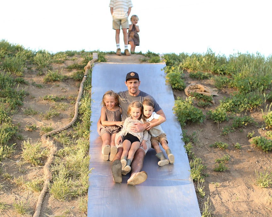 Family enjoying outdoor activities on a farm, highlighting Primal Pastures' commitment to sustainable farming and grass-fed meats, with lush greenery in the background.