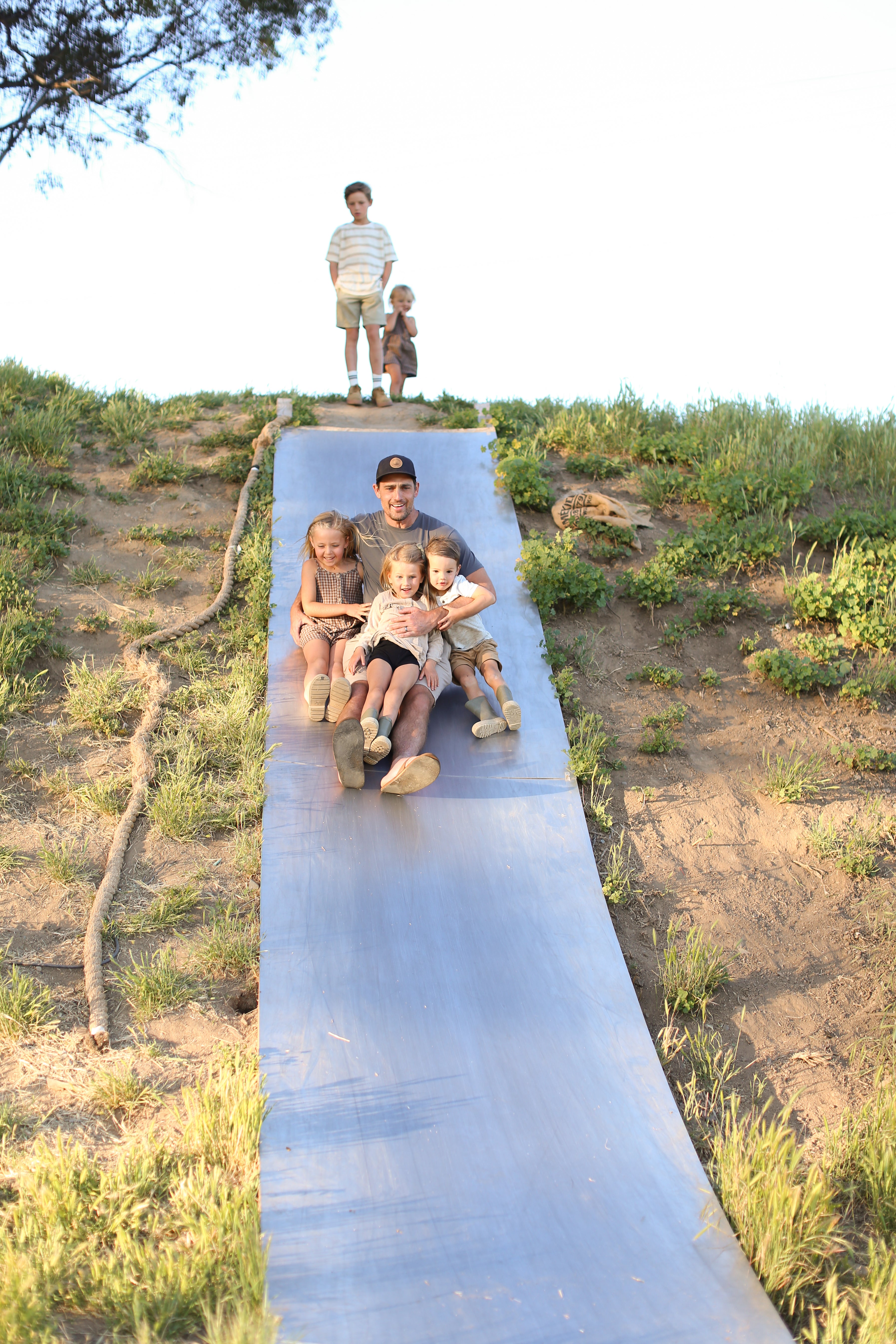 Family sliding down a long metal slide in a natural setting