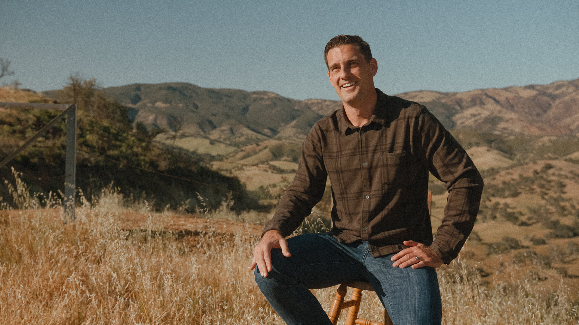 Man sitting on a stool in a field with mountains in the background