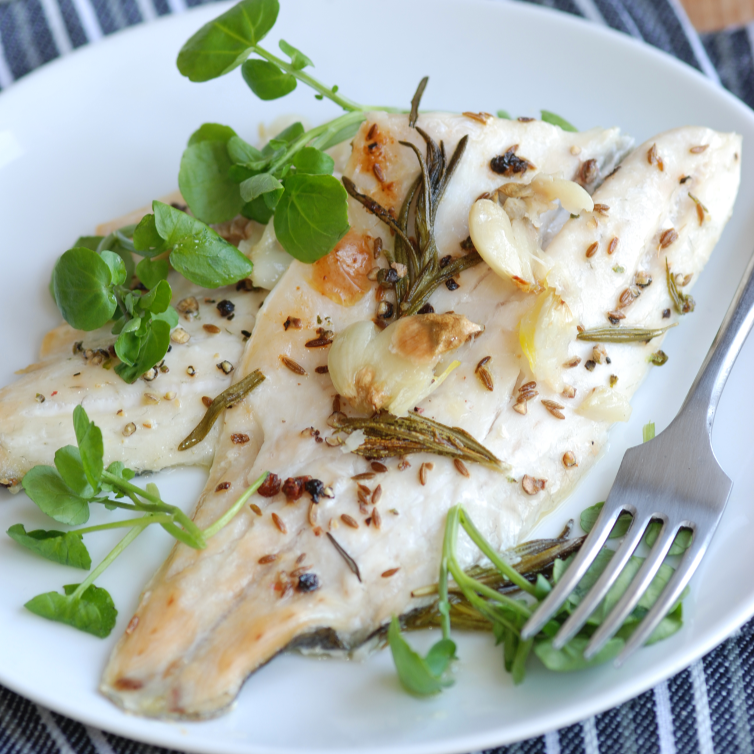 A plate containing cooked white sea bass garnished with herbs and a side salad.