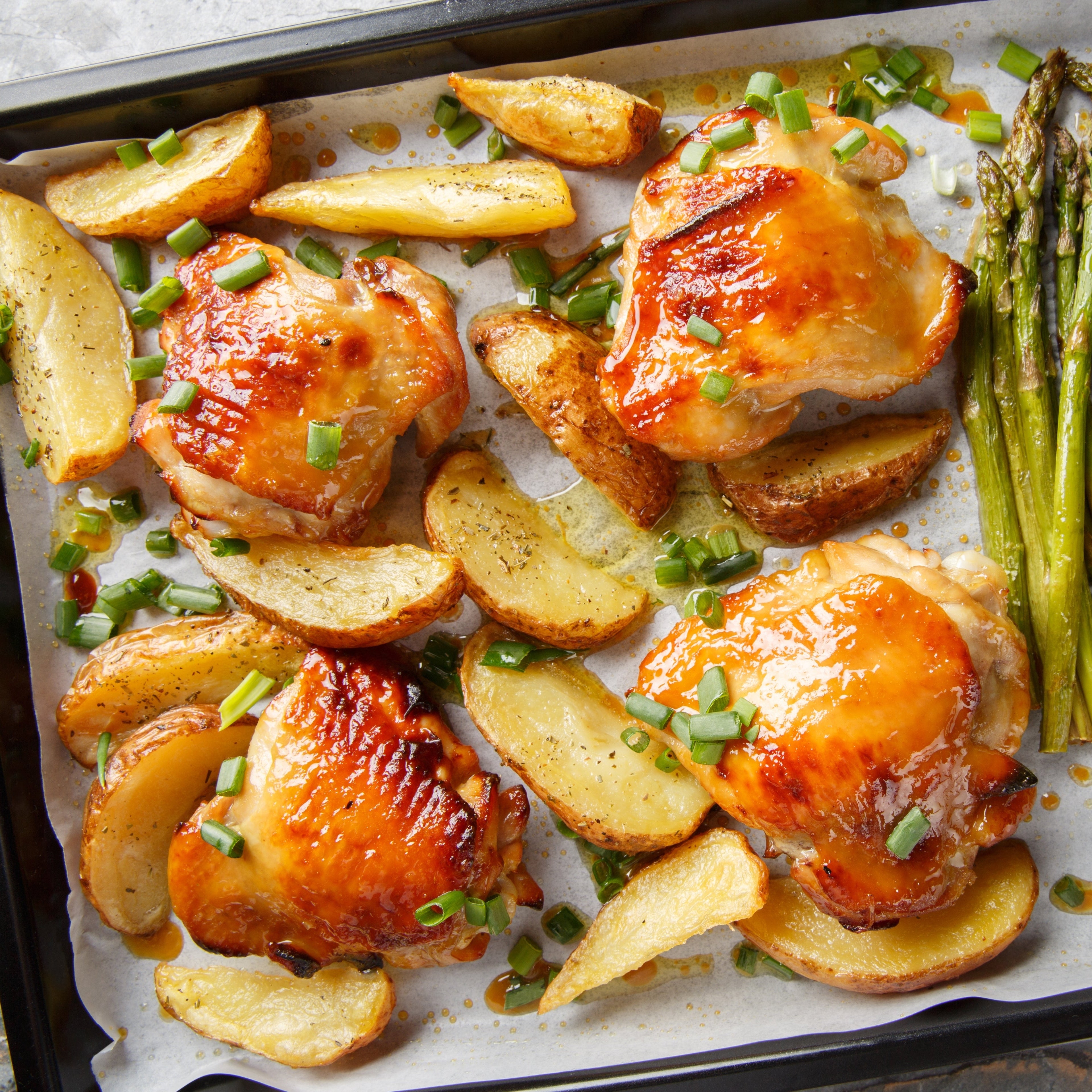 Baked chicken thighs with potatoes and asparagus on a baking tray.