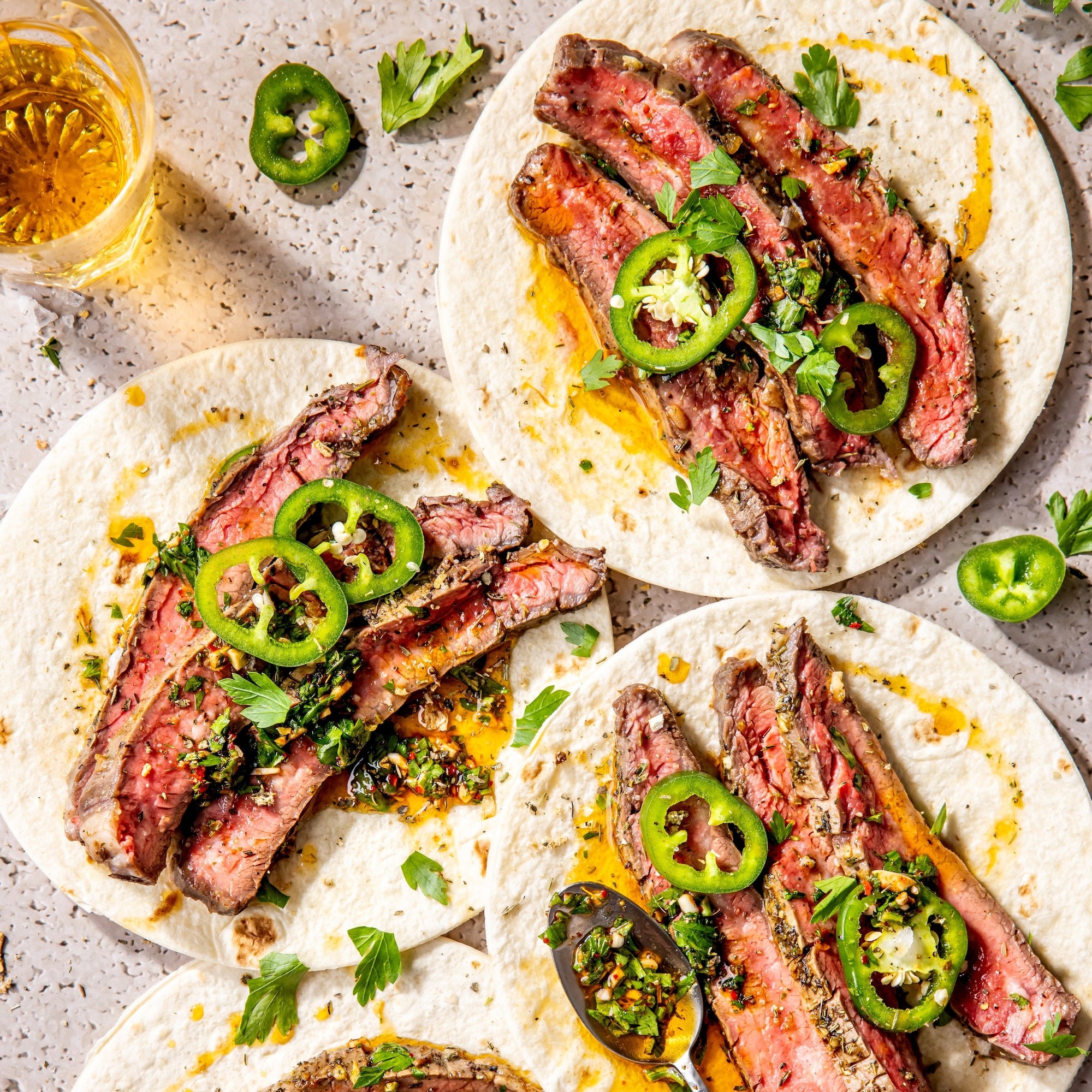 Steak tacos with jalapeños and a glass of beer on a stone surface