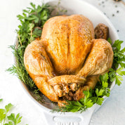 Roasted chicken on a bed of greens in a white bowl with a white background


