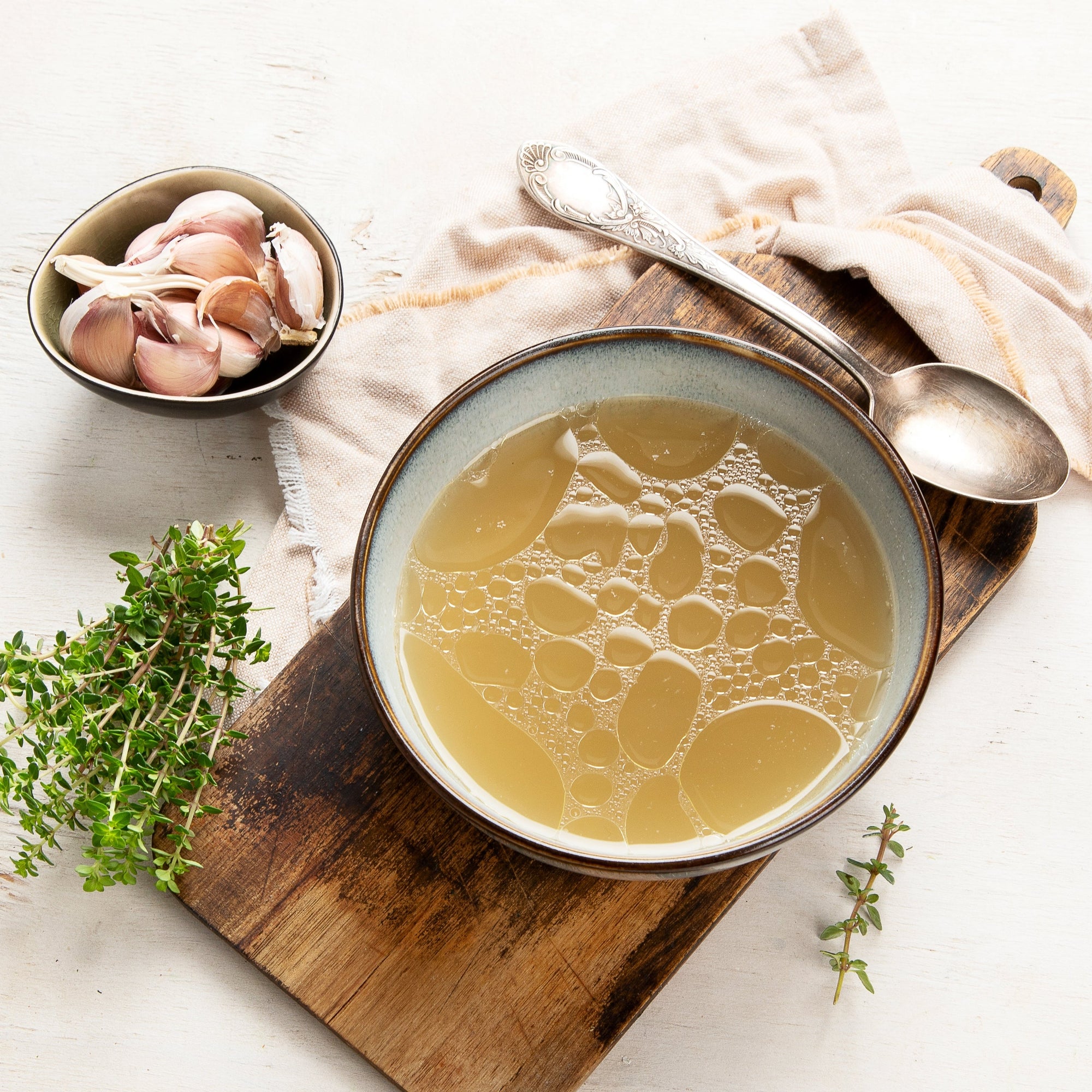 Bowl of soup on a wooden board with herbs and a cloth napkin.
