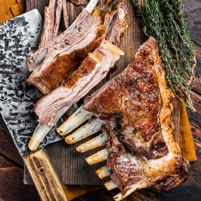 Cooked lamb spare ribs on a wooden cutting board with a cleaver and thyme in the background.