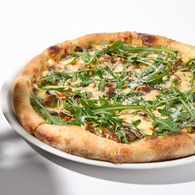 A pizza topped with ground Italian chicken sausage, cheese, and arugula, served on a white plate.
