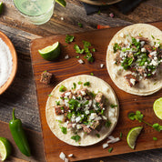 A prepared dish consisting of beef tongue tacos served with various toppings and sides, presented on a wooden cutting board.