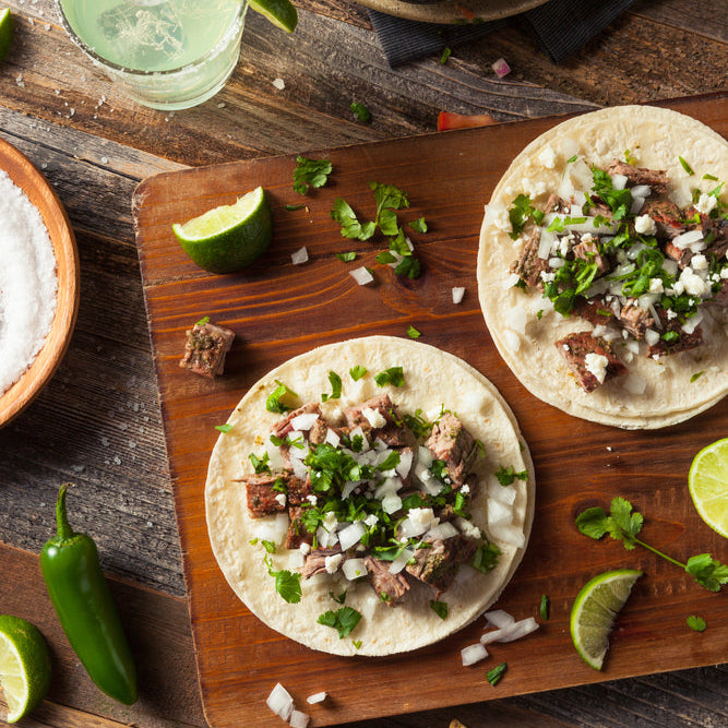 A prepared dish consisting of beef tongue tacos served with various toppings and sides, presented on a wooden cutting board.