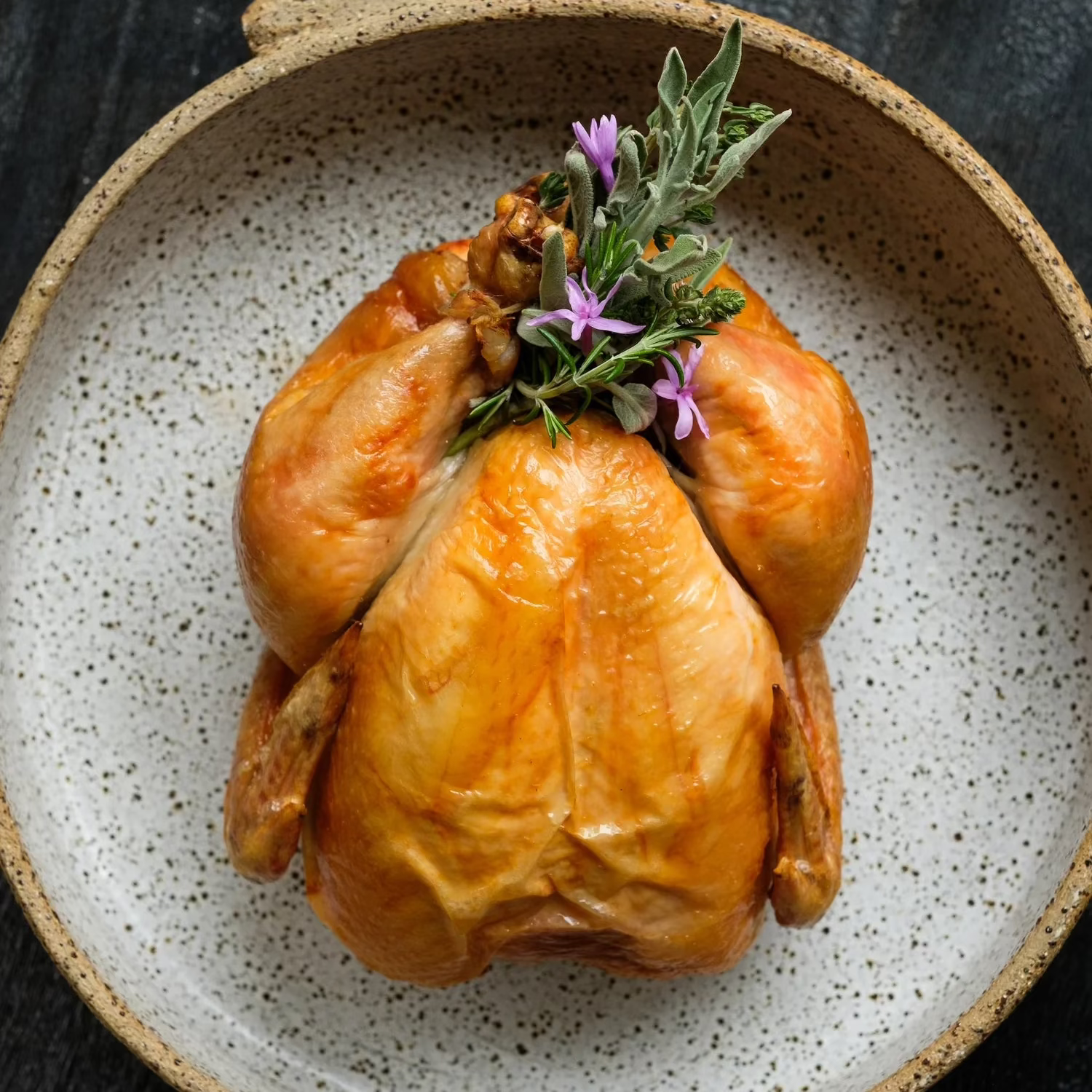 A delicious-looking roasted whole chicken on a plate, prepared with a garnish.