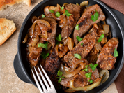 A skillet filled with tender, pan-fried grass-fed beef liver, garnished with sautéed onions and fresh parsley.