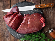 Freshly sliced grass-fed beef liver on a black slate board, accompanied by a knife and garnished with dill.