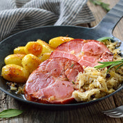 Sliced ham steaks in a skillet with potatoes and herbs.